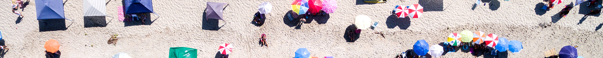 aerial shot of a beach with people playing in the surf and colorful umbrellas on the sand